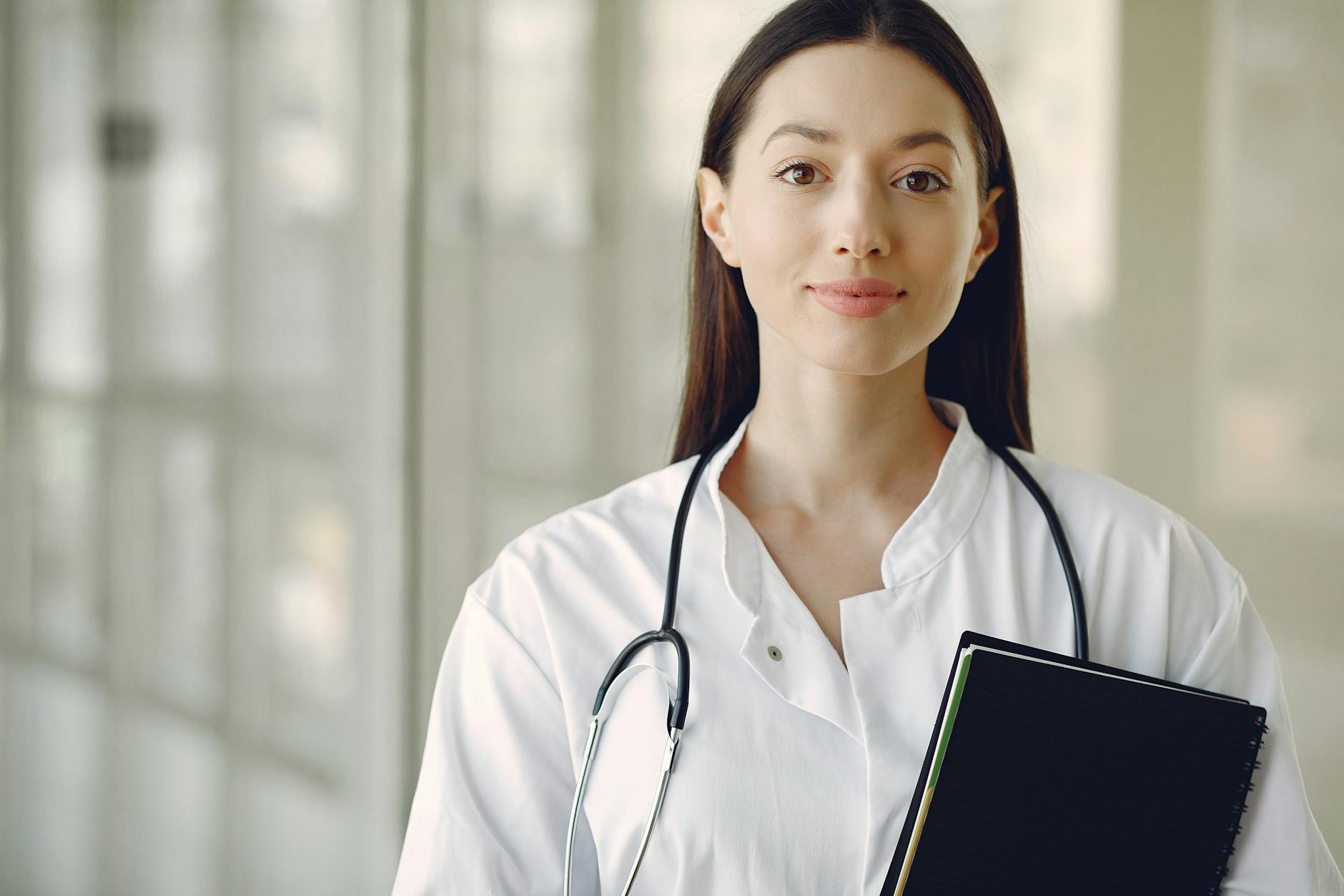 young doctor in uniform with stethoscope and notebook in medical room